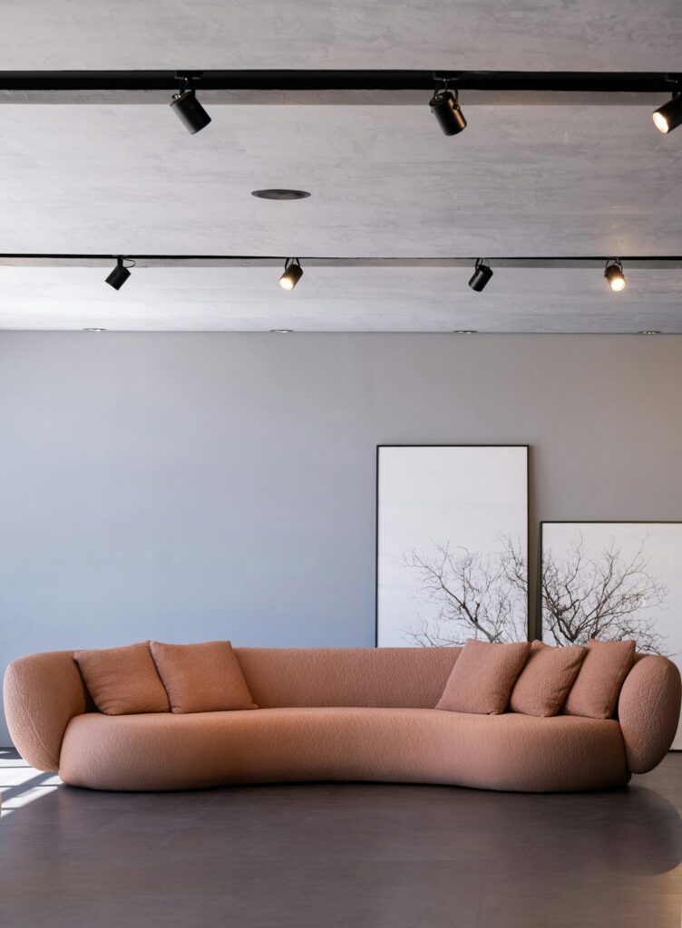 Długa sofa boucle w przygaszonym różowym kolorze z zaokrąglonymi podłokietnikami.